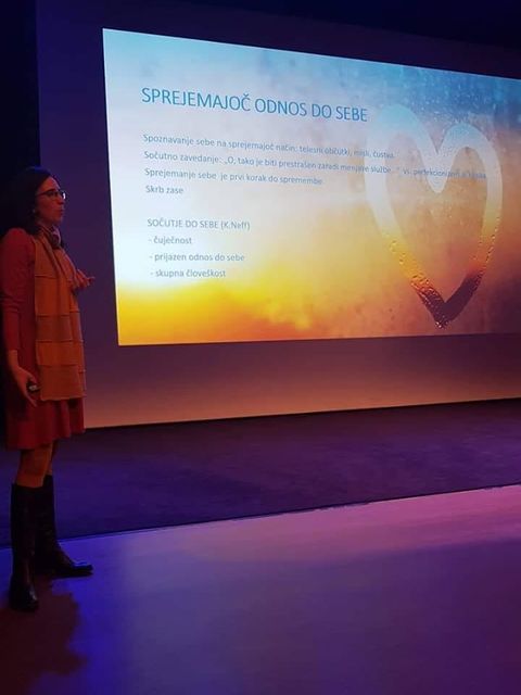 Maja Bajt med predavanjem 'Sprejemajoč odnos do sebe' pred platnom s predstavitvijo.